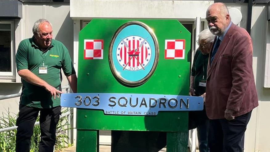 Two men holding the 303 Squadron plate which will be installed on the locomotive