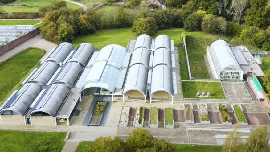 An aerial image of the Millennium Seed Bank at Wakehurst made up of a number of white and grey greehouse style buildings set among lush greenery