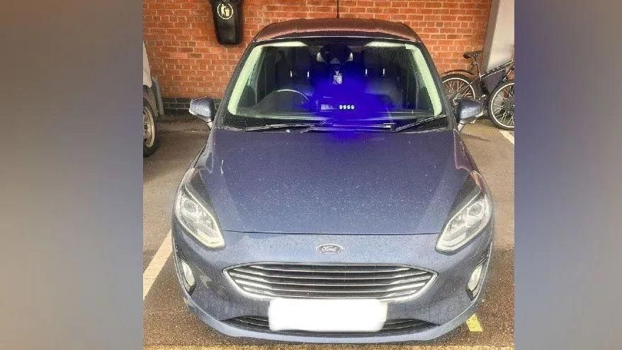 Blue Ford car with blue light positioned near front windscreen. The car is parked in a garage and has the number plate blocked off.