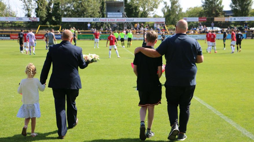 Southport FC director Steve Porter and his granddaughter (left) carry a wreath onto the pitch alongside FC United of Manchester chairman Nick Boom and FCUM junior member Alfie Marran-Jones