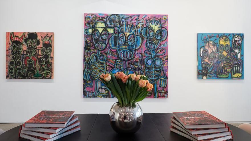 Three Aboudia paintings hung in a gallery. Copies of his monograph sit on a table in the foreground.