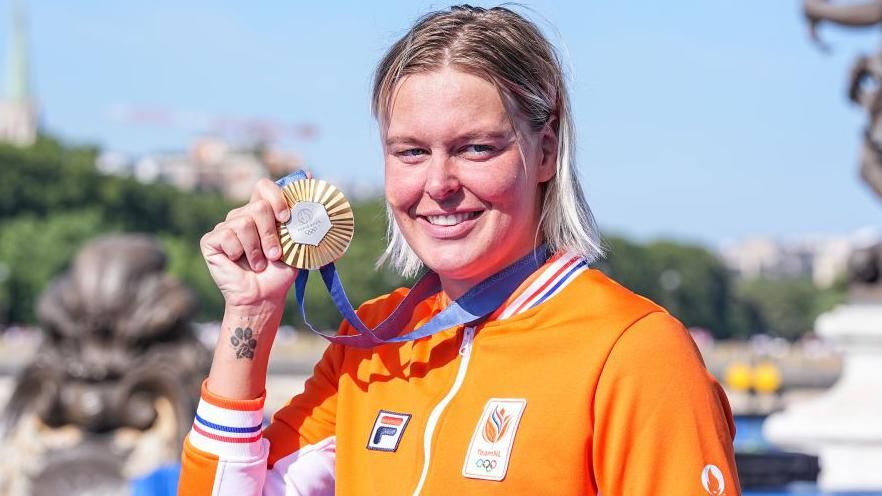 Sharon van Rouwendaal holds her gold medal up with a paw print tattoo on her wrist visible