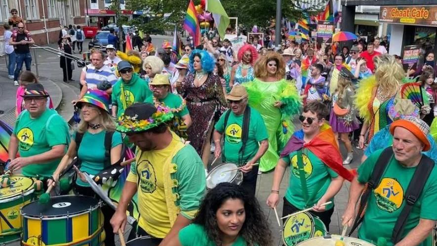 Parade with samba band and many people dressed in rainbow behind