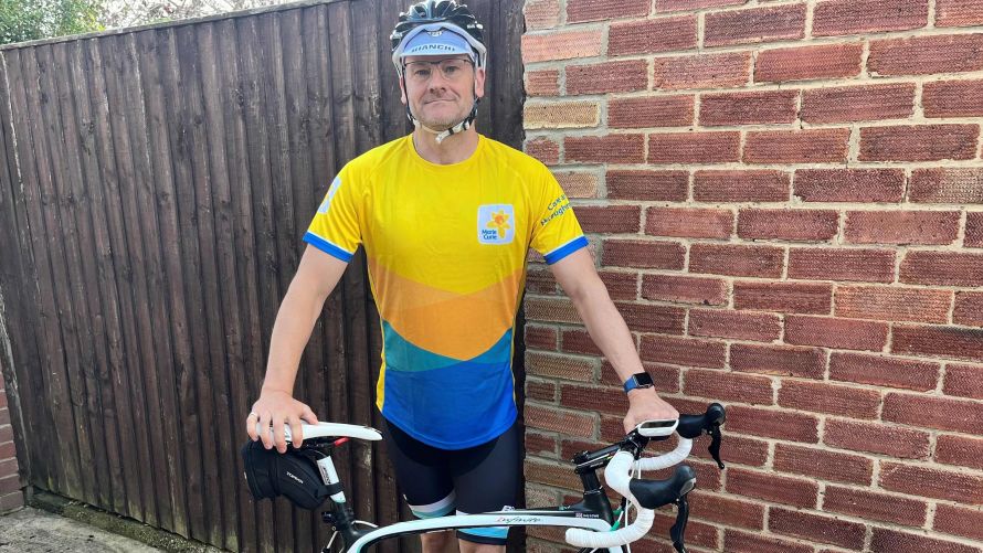 Man wearing a yellow top and shorts, standing next to a bicycle and wearing a safety helmet