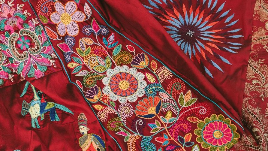 A close up image of brighly coloured flowers, animals and human figures on a red dress