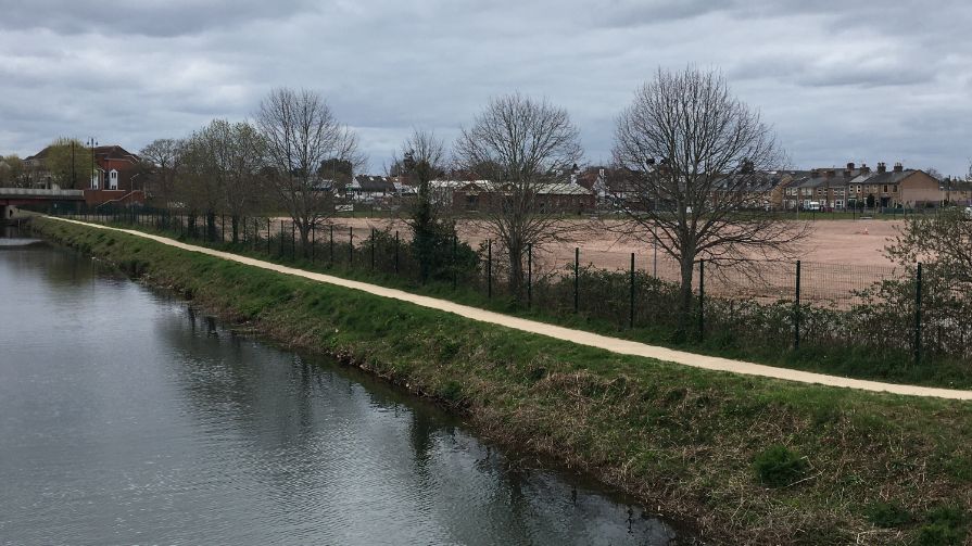 A river with a cycle path and a vacant brownfield site beyond