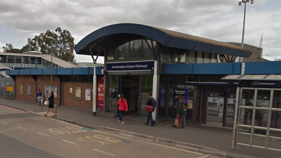 Entrance to Southampton Airport Parkway train station, a building with a curved roof. There are several people walking around outside.