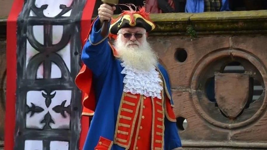 Town crier Martin Wood in blue, red and gold regalia, ringing a bell