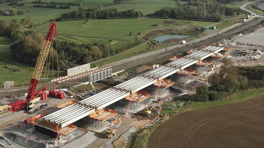 Viaduct in countryside, showing seven spans each made up of four light grey beams supported on pillars. A large red and yellow crane is visible in the foreground.