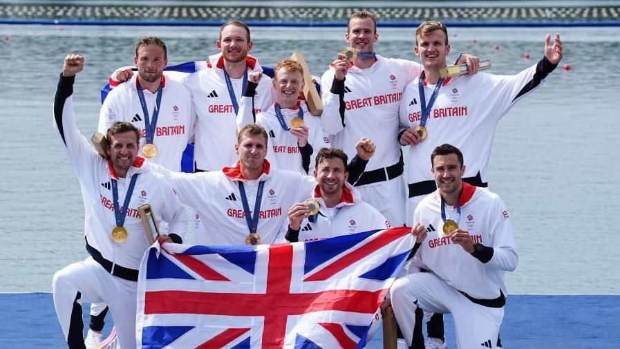 The men's eight Team GB rowing crew smile as they hold up their gold medals