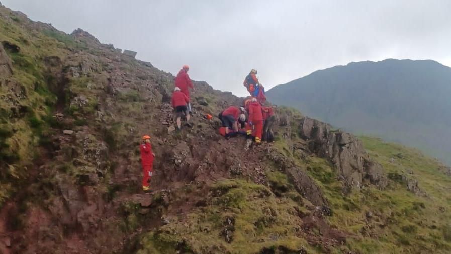 A mountain rescue team wearing red uniforms are seen attending to Lyn at the scene. 
