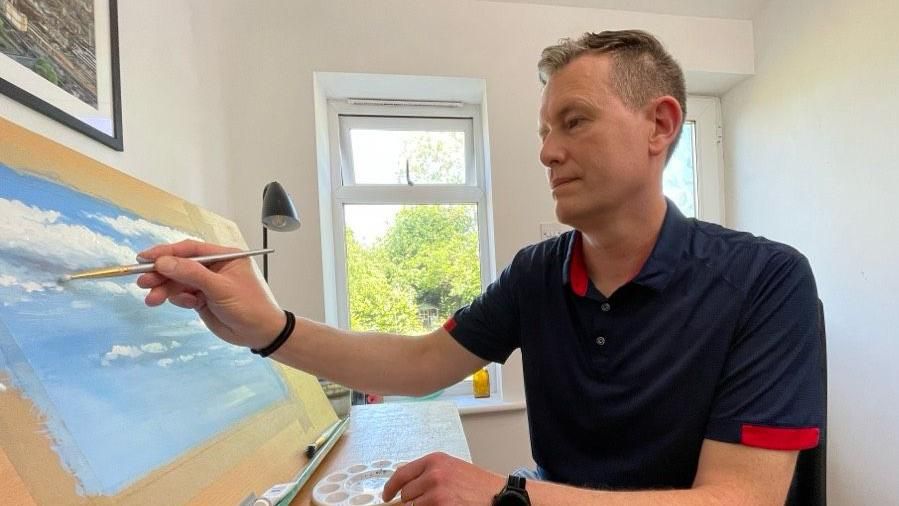 Matthew Emeny painting a blue sky with white clouds
