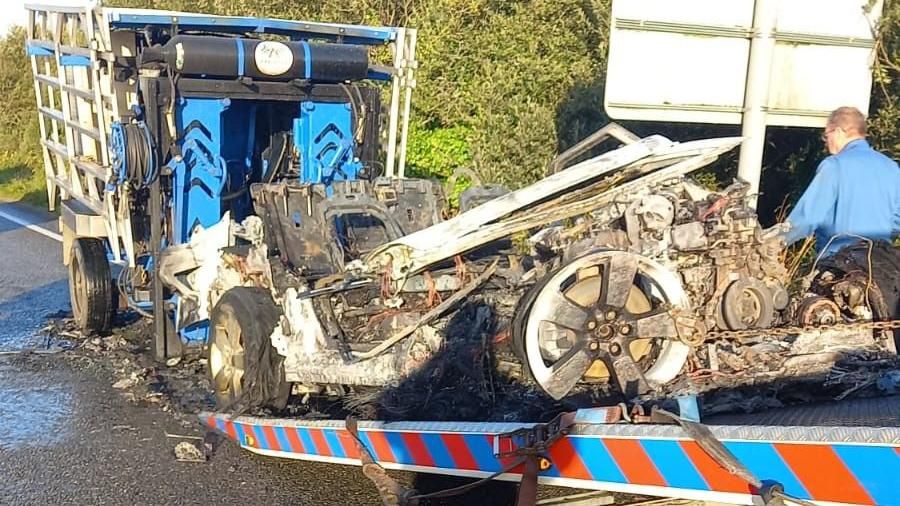 The aftermath of the fire shows a mangled metal on a trailer with burnt tyres and twisted debris.