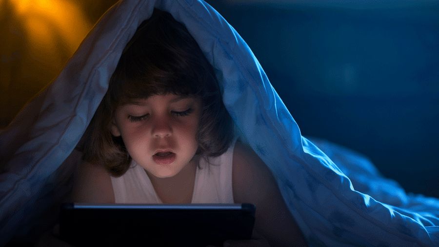 Child on tablet under blanket