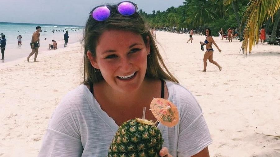Emily Oliver on a sandy beach, smiling and holding a pineapple
