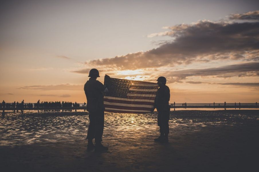 People dressed as US soldiers hold the US flag on Omaha beach