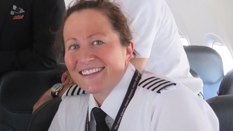  Kate Newton smiling while wearing her pilot uniform on plane.