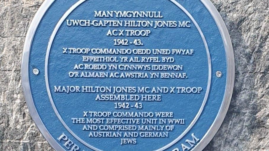 Circular blue plaque with text in Welsh English and Latin
