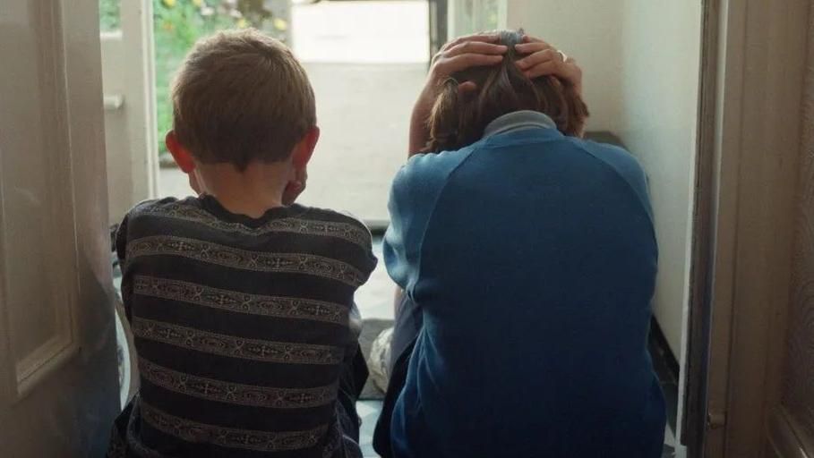 Two young children sat on the floor. Their backs are turned to the camera and they are sat with their heads in their hands. 