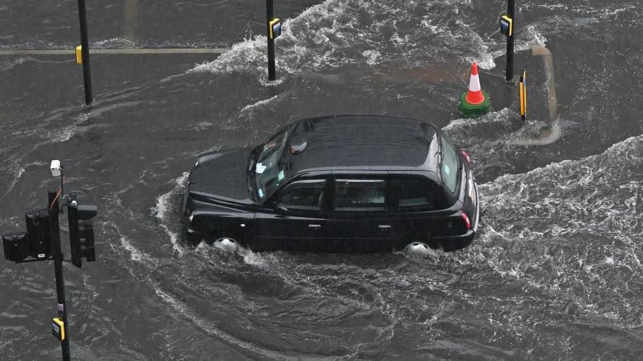 A black cab drives through flooded road