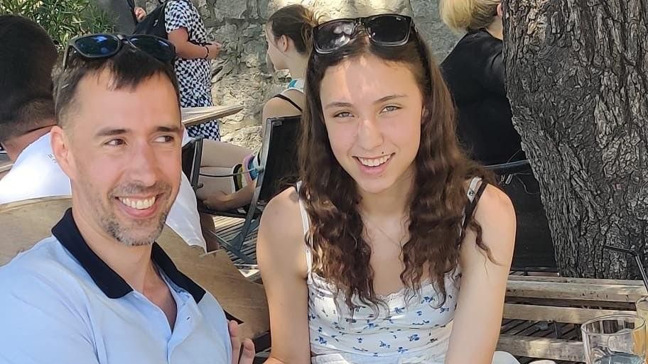 Sqn Ldr Mark Long with eldest daughter Scarlett. They are smiling and wearing sunglasses on the tops of their heads. He wears a blue polo shirt and she wears a patterned summer top.