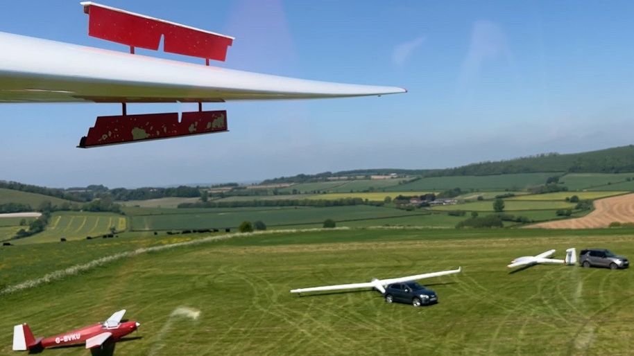 A glider coming into land with grounded planes pictured underneath it's descending wing