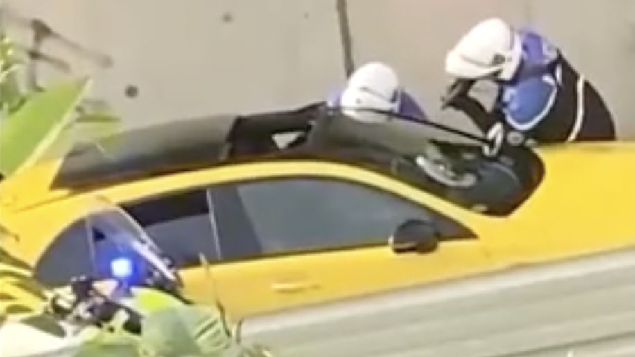 A screen grab of a video shared online showing a yellow car with a police officer pointing a gun at the driver