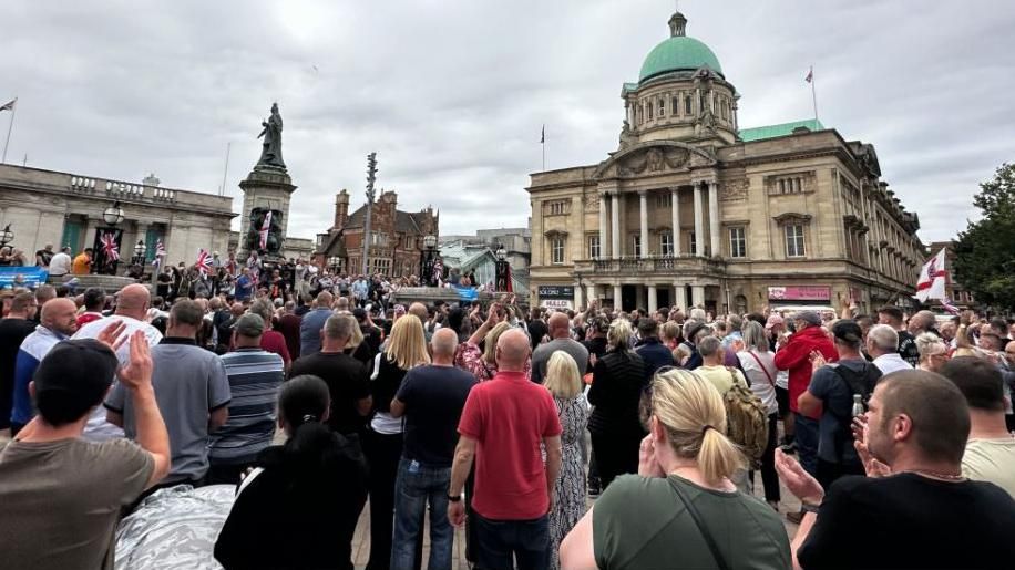 Hundreds of people standing in Queen Victoria Square, Hull, with some holding Cross of St George and Union flags.