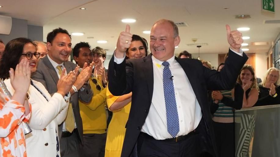 Sir Ed Davey giving a thumbs up in front of a jubilant set of supporters