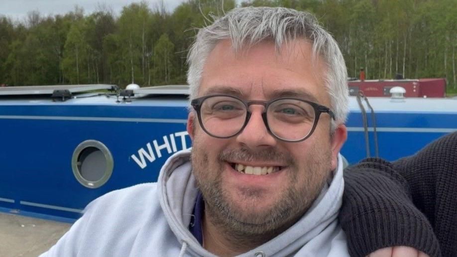 Mr Auty has glasses and short grey hair. He is smiling at the camera.