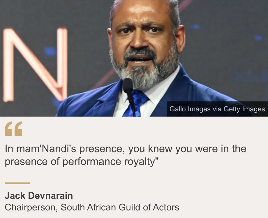 "In mam'Nandi's presence, you knew you were in the presence of performance royalty"", Source: Jack Devnarain, Source description: Chairperson, South African Guild of Actors, Image: Jack Devnarain wearing a blue suit and tie speaks at a microphone.
