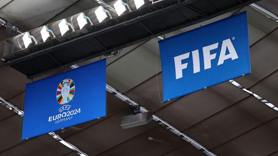Euro 2024 and Fifa flags hanging from a stadium roof
