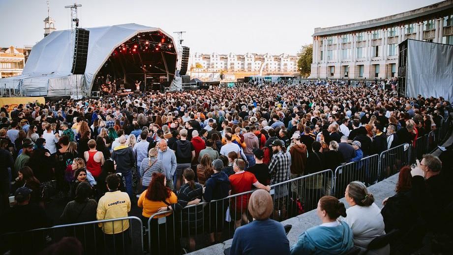 A large crowd watch Placebo at Bristol Sounds 2024 with the Lloyds Ampitheatre building visible in the background