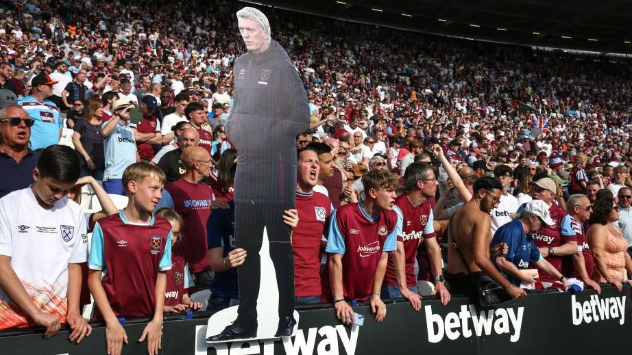 A fan holds up a cardboard cut out of David Moyes