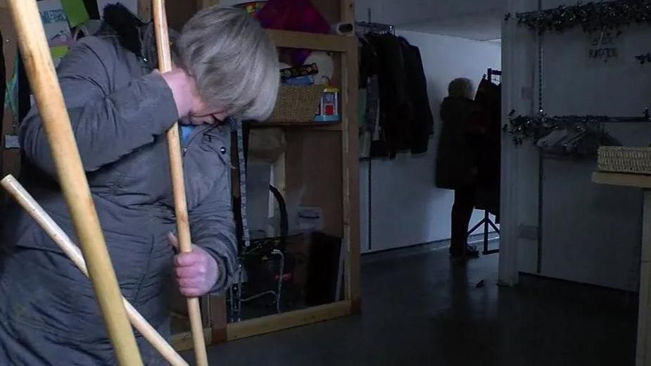 A woman, wearing a grey winter coat and with grey short hair, mops a flooded shop in Padiham after the town was flooded