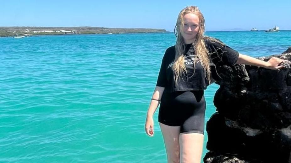 Mollie Mulheron posing in front of the sea, wearing black shorts and a T-shirt