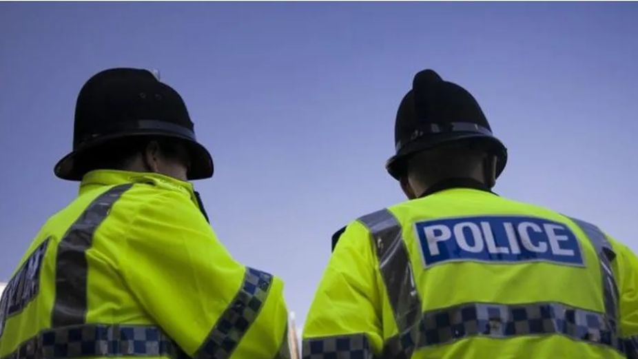 Two police officers wearing a bright yellow jacket with the words POLICE  in bold white lettering in a blue rectangle 