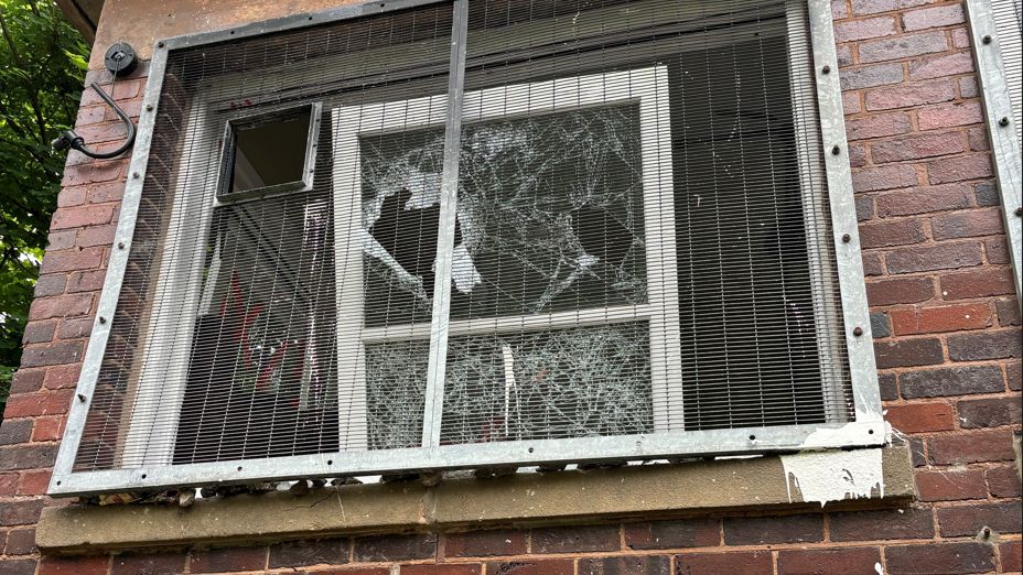 A window which has a cage on the outside. It has been smashed from the inside