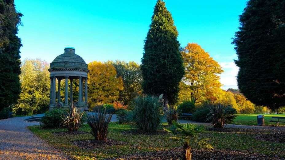 Roundhay Park with trees and plants in the foreground and a bandstand-style structure