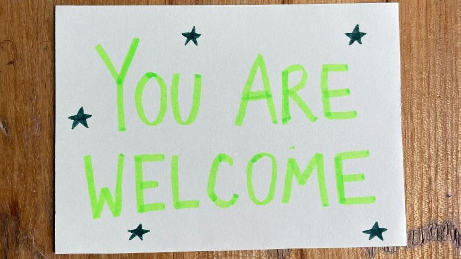 A hand-drawn sign reads you are welcome in green. 