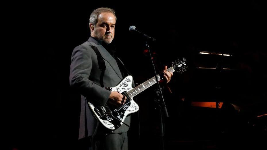 David Arnold playing a signed white electric guitar on stage