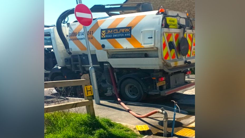 JM Clark truck with a hose leading to a water pipe on a pavement