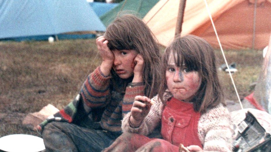 Two children sitting on the ground with tents behind them