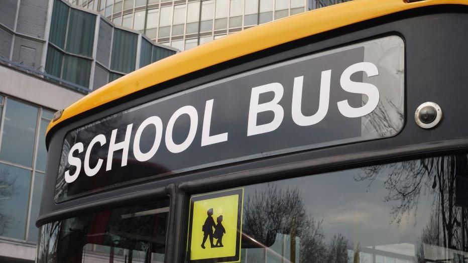 Picture of the front of bus which says school bus and a school children sign just below at the top right corner of the window on the left