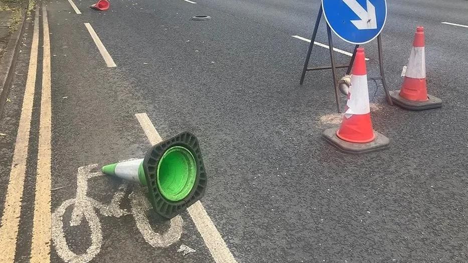 A green cone, lying on its side - part of a series of cycle lanes on the A56 in Stretford