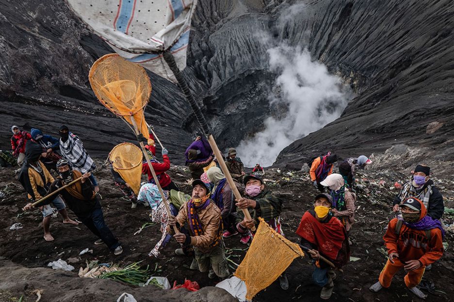 A group of people stand on the edge of a volcano with long nets