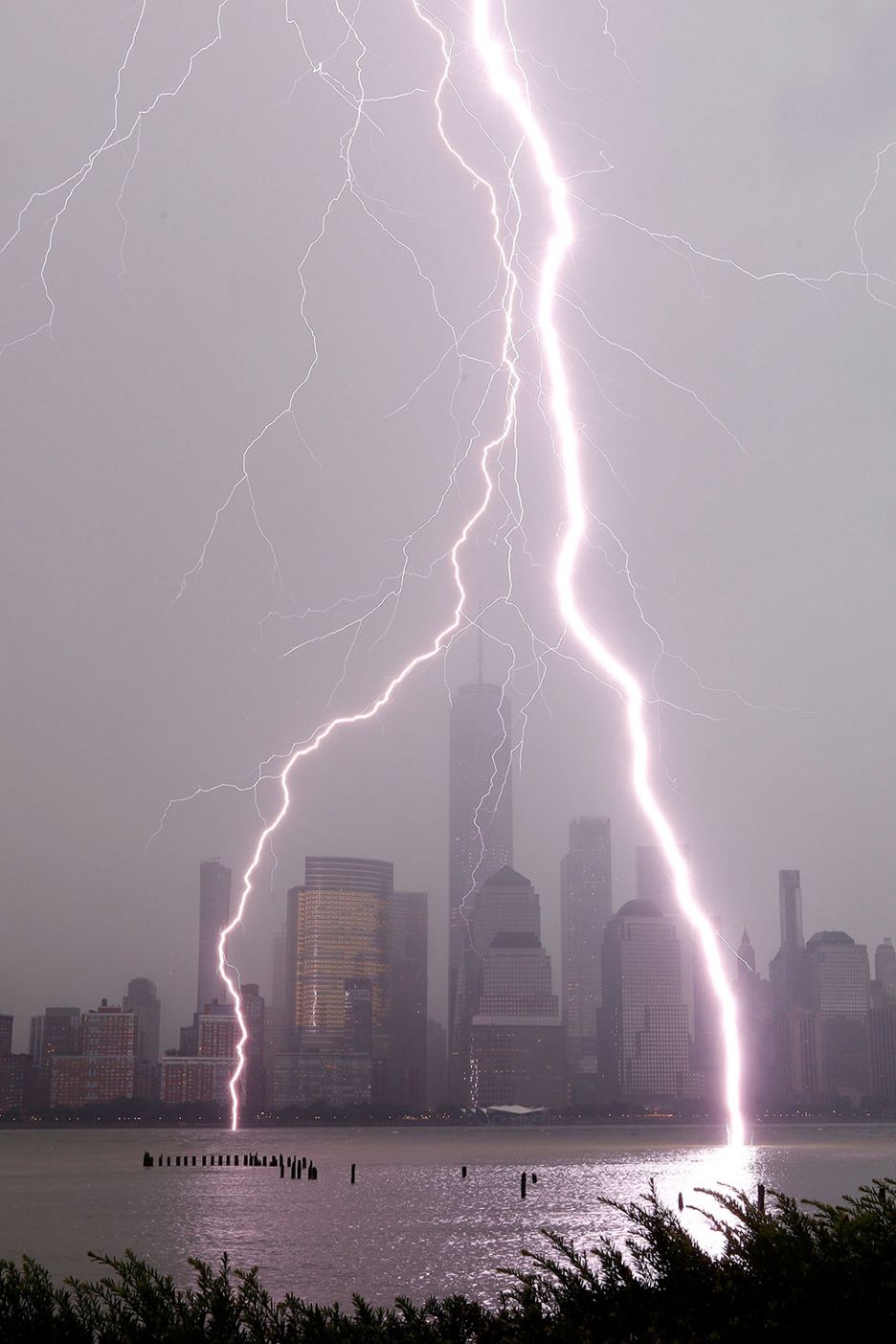 Lightning bolts hit a river with a city skyline behind