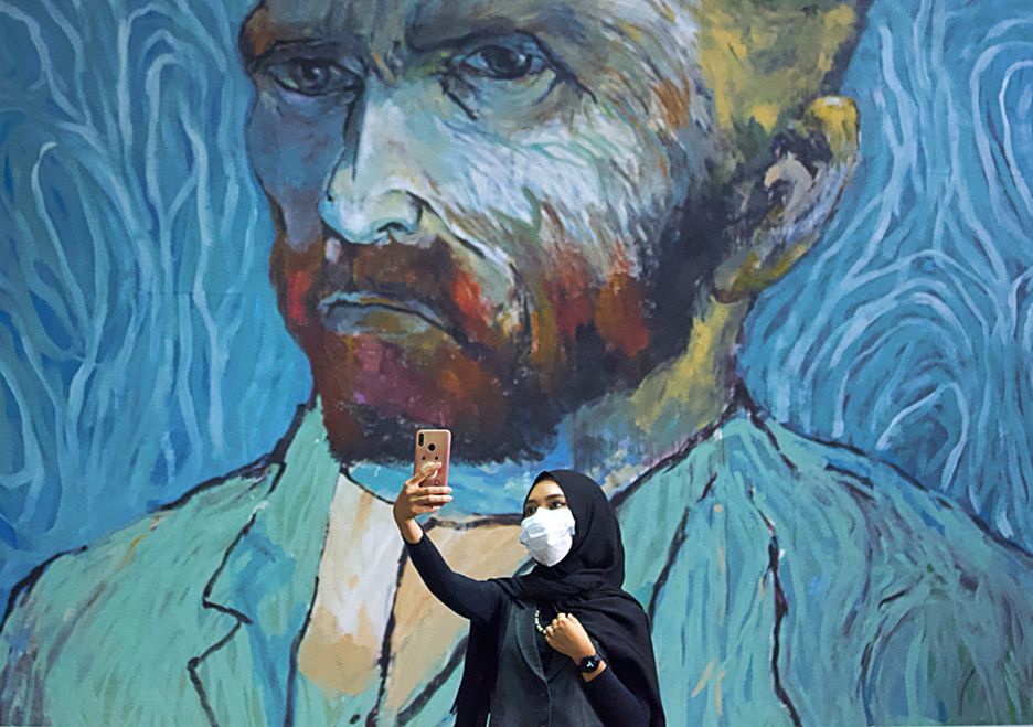 A woman takes a selfie with a large mural of Van Gogh