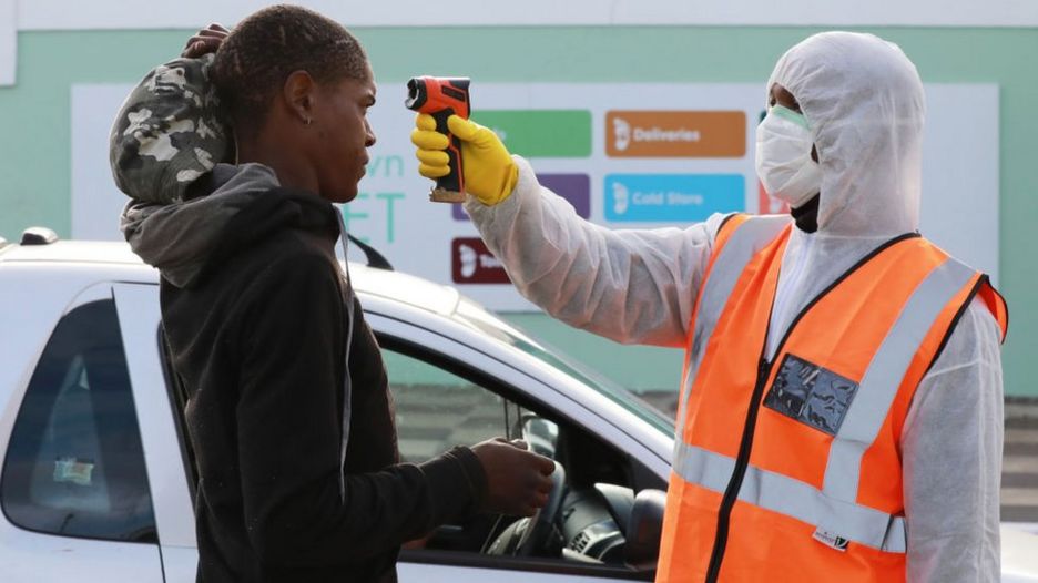 Profissional de saúde faz medição de temperatura de mulher na África do Sul