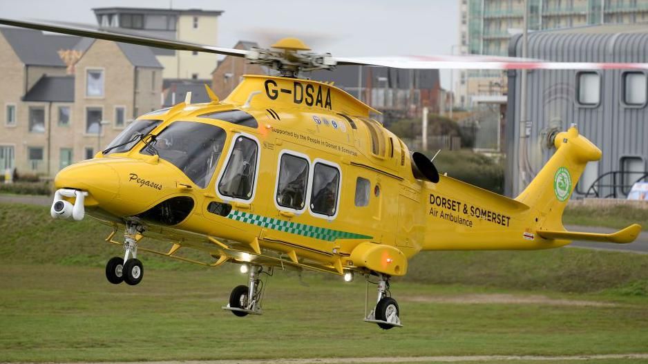 Dorset and Somerset air ambluance taking off from a field. It's a yellow ambulance with the logo on the tail